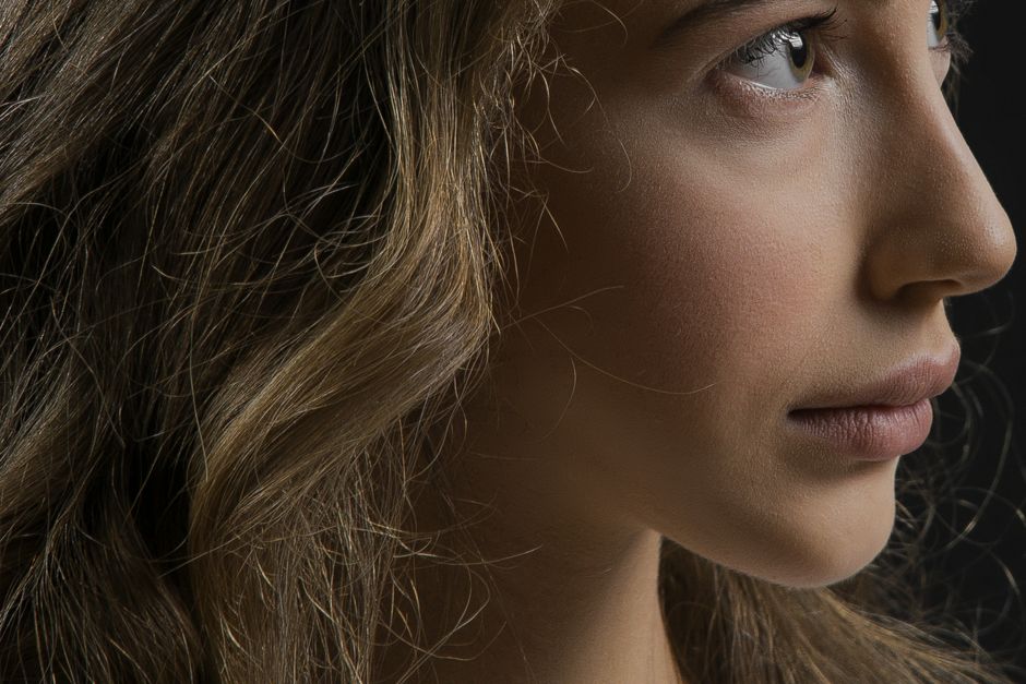 Retrato de perfil de una mujer joven con el pelo ondulado sobre fondo oscuro