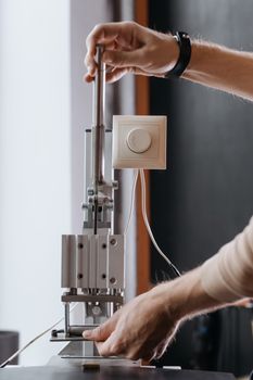 Hands adjusting a lever on a machine in an indoor setting, showcasing precise manual work.