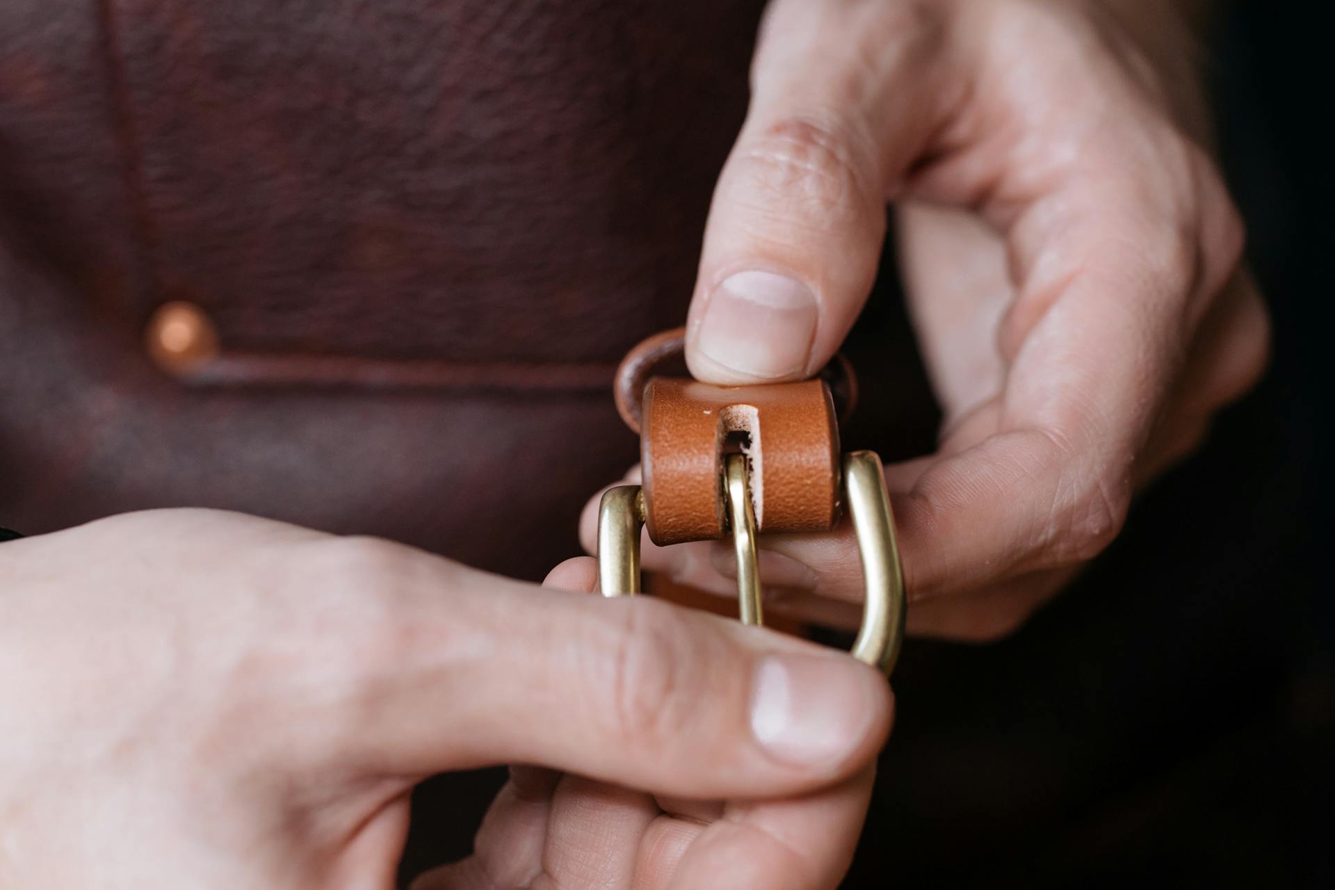 A Person Holding the Buckle of a Brown Leather Belt