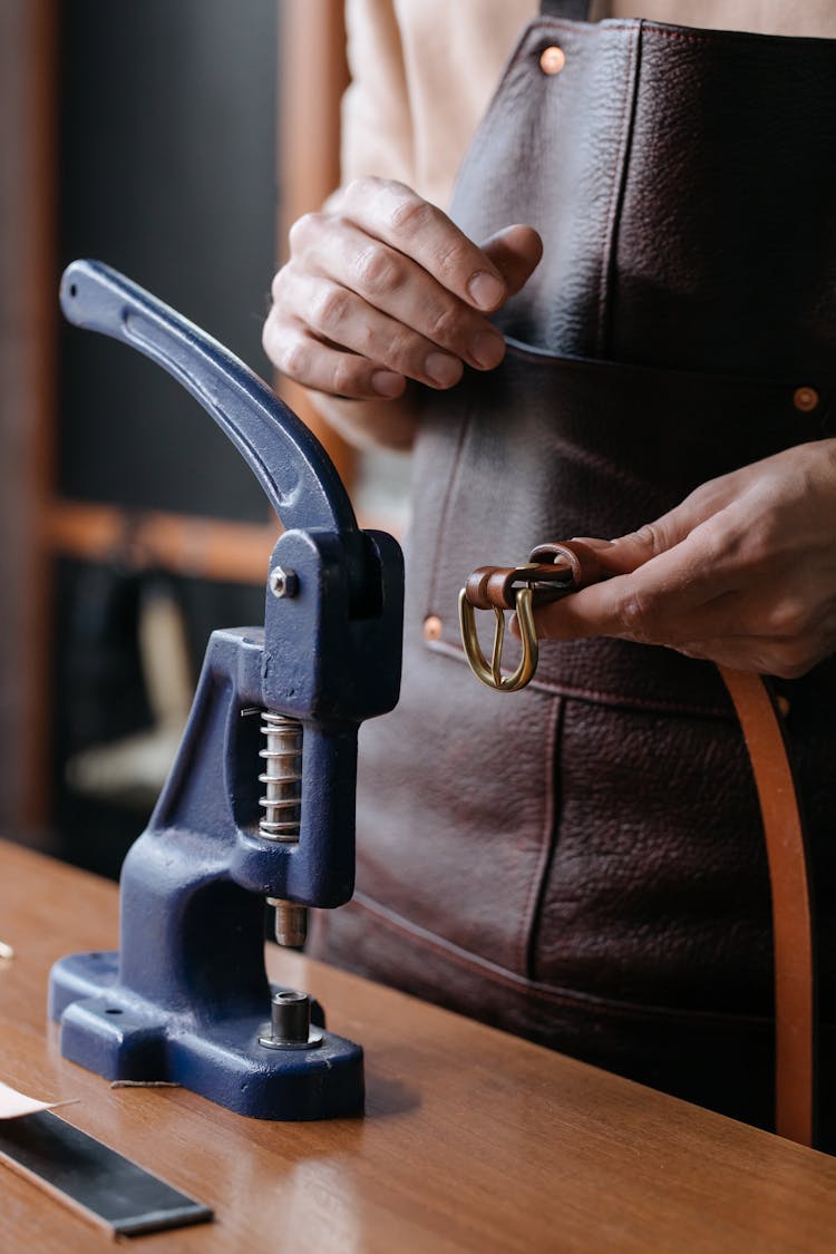 A Person Holding A Brown Leather Belt Near A Metal Stud Fastener