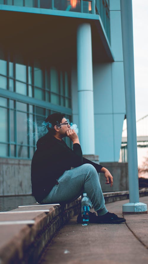 Free A Man in Black Hoodie Jacket Sitting on Pavement Smoking Stock Photo