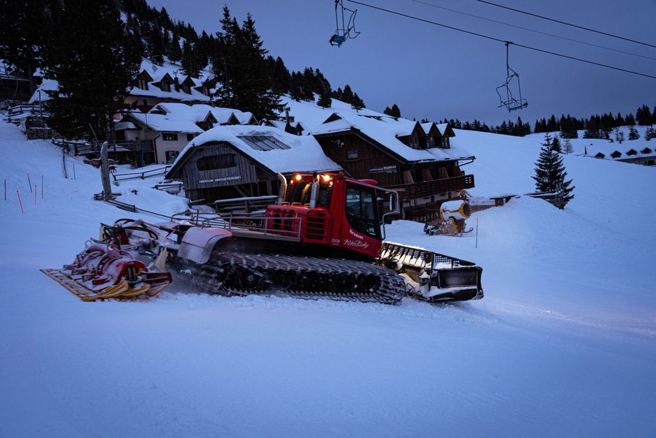 A powerful snow groomer preparing ski slopes at a winter resort during twilight.