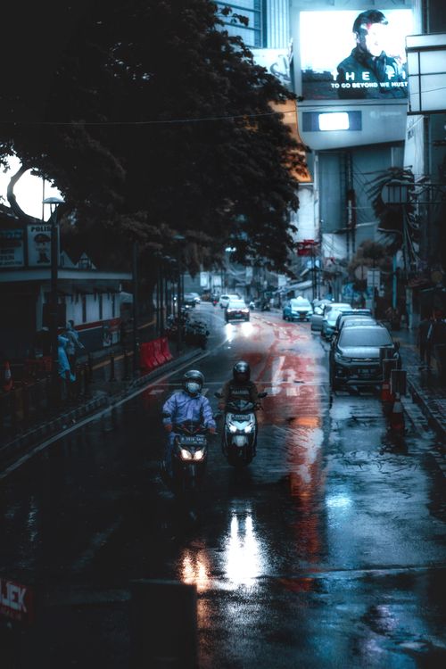 Free Motor scooters on a wet street in Jakarta city during the day, showcasing urban life. Stock Photo
