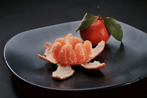 Free Close-up of a juicy peeled tangerine with leaves on a modern black plate. Stock Photo