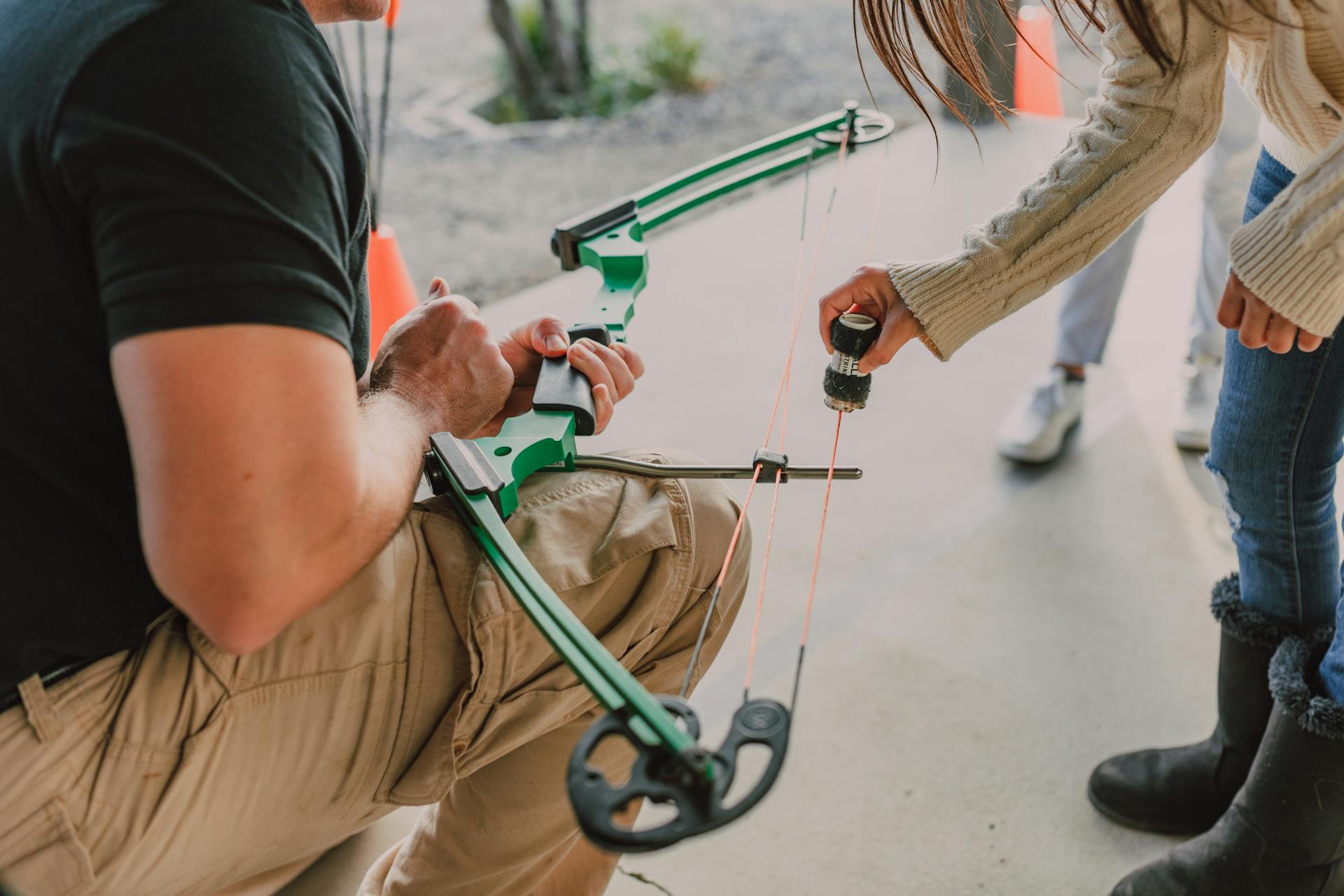 Man Holding A Bow While A Girl Is Waxing The Bowstring