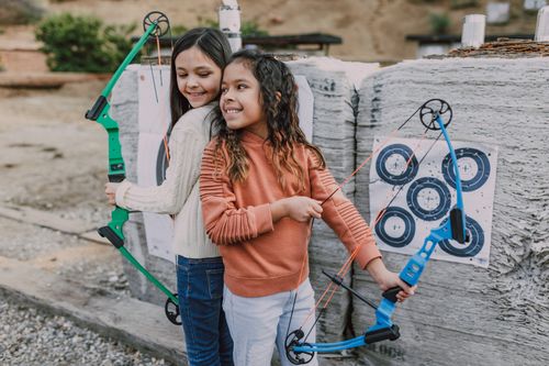 Free Two girls with bows smiling during archery practice outdoors. Stock Photo
