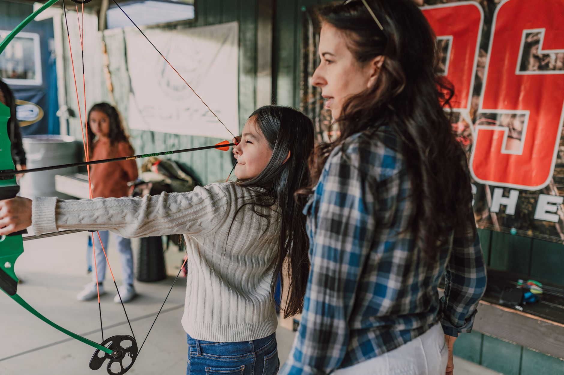 Young girl learning archery with guidance, capturing focus and precision in an outdoor setting.