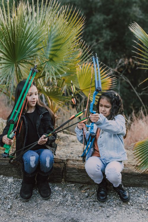 Free Two young girls practicing archery outdoors, holding compound bows in a natural setting. Stock Photo