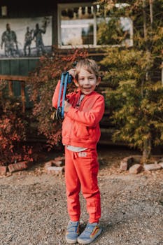 A smiling boy holds a toy bow outdoors in a casual archery setup, enjoying a fall day.