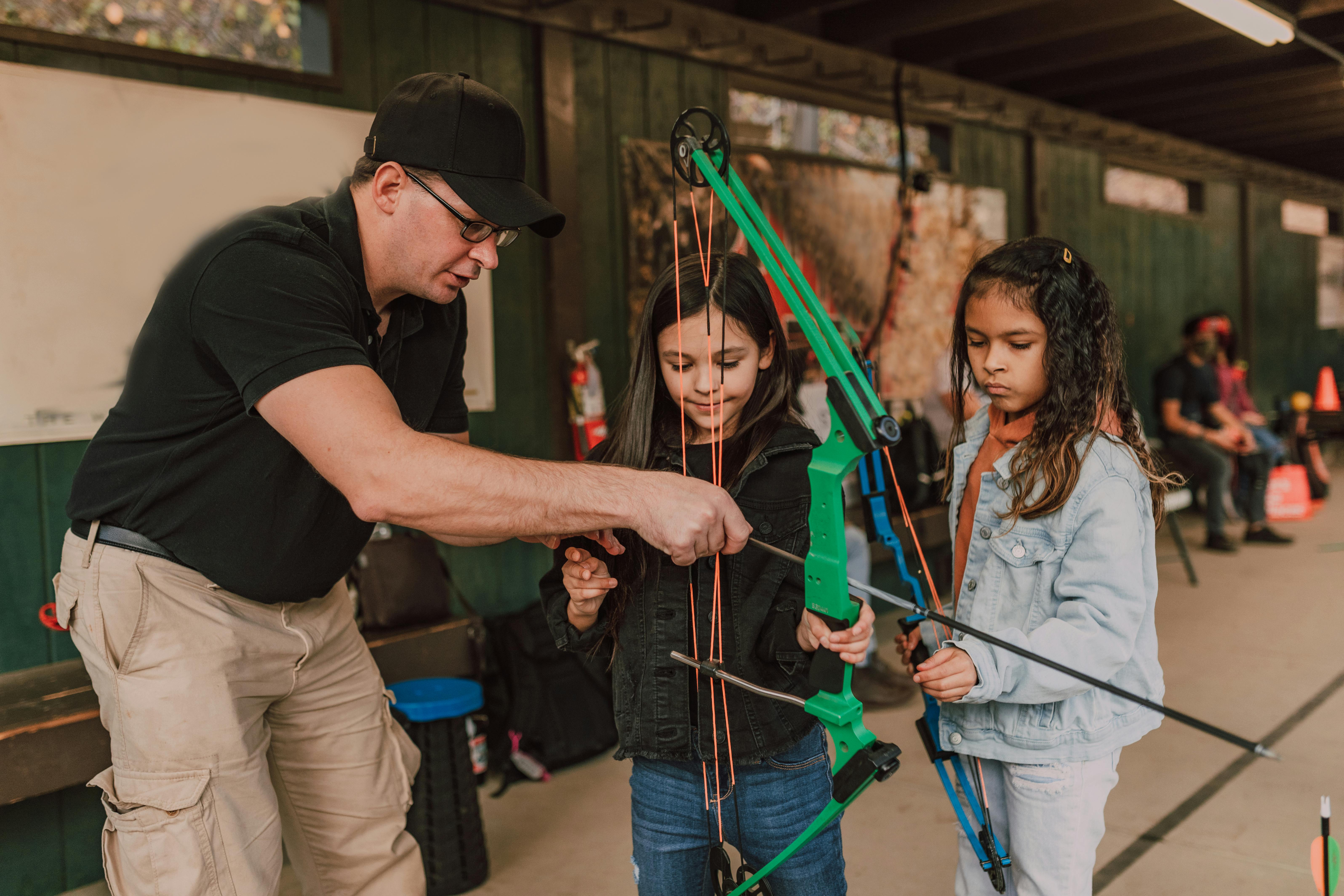 cute attentive diverse little girl practicing archery with male instructor