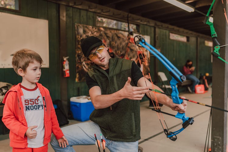 A Man Teaching A Boy How To Hold The Bow And Arrow