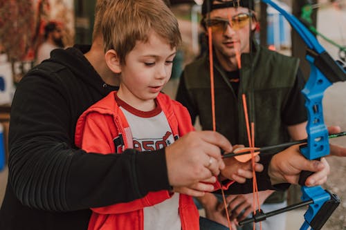 A Person Teaching a Boy How to Put the Arrow on the Bow