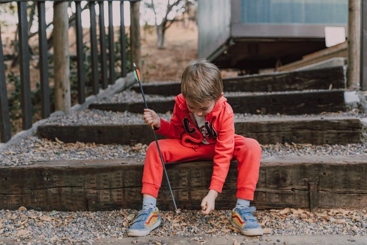 A Boy Sitting On The Stairs Holding An Arrow