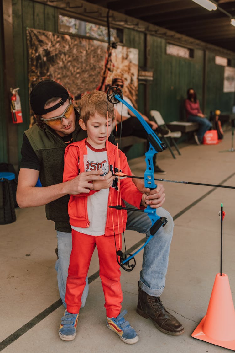 A Man Teaching A Boy How To Pull The String Of A Bow