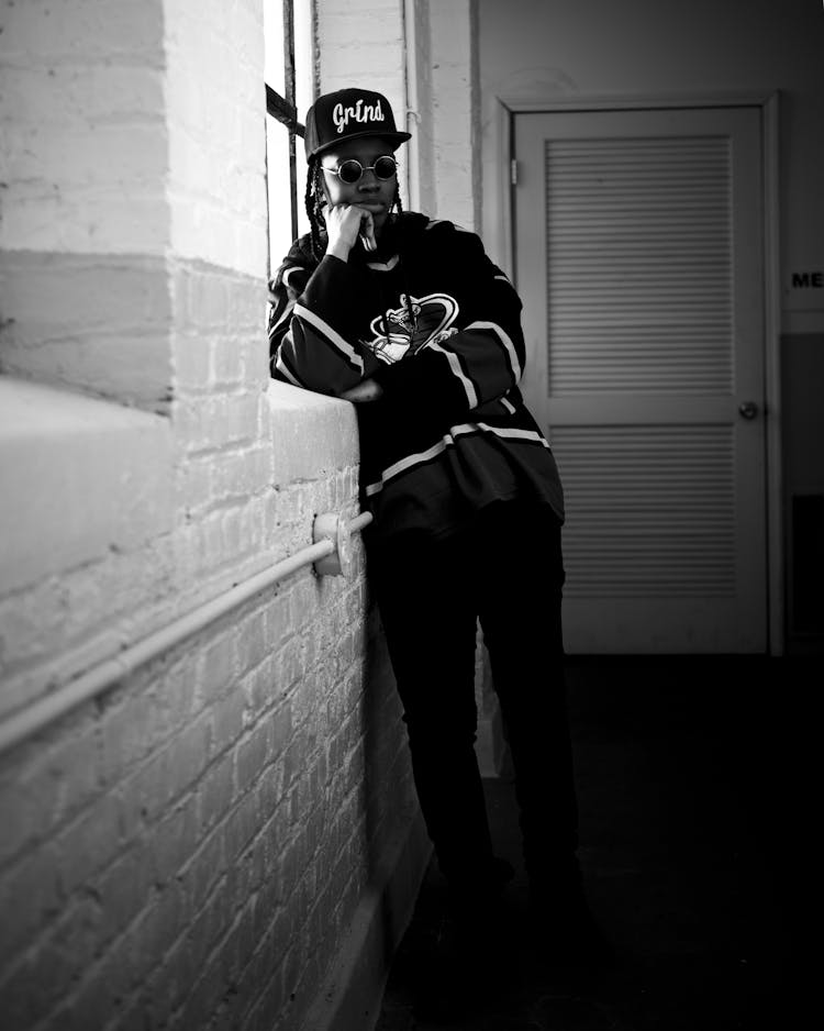 Man In Baseball Cap And Sunglasses Leaning Against A Wall 