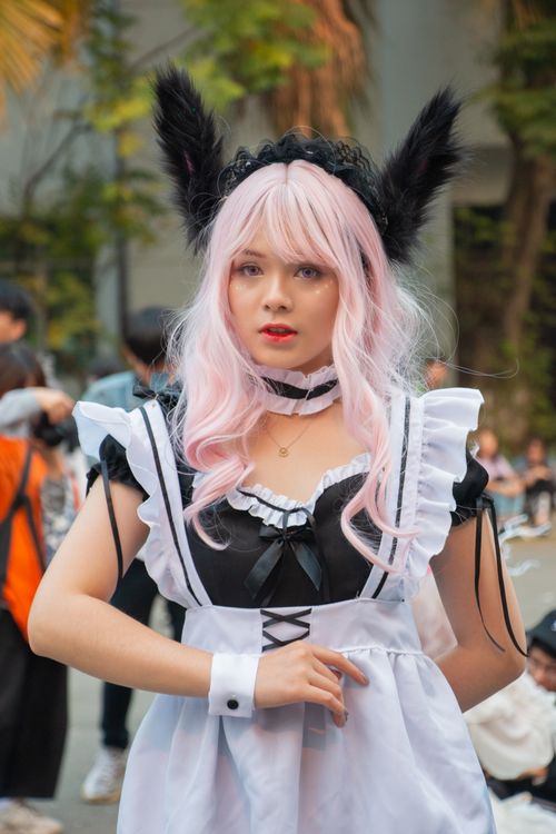 Free Young woman in a cosplay costume with pink wig and black dress at an event. Stock Photo