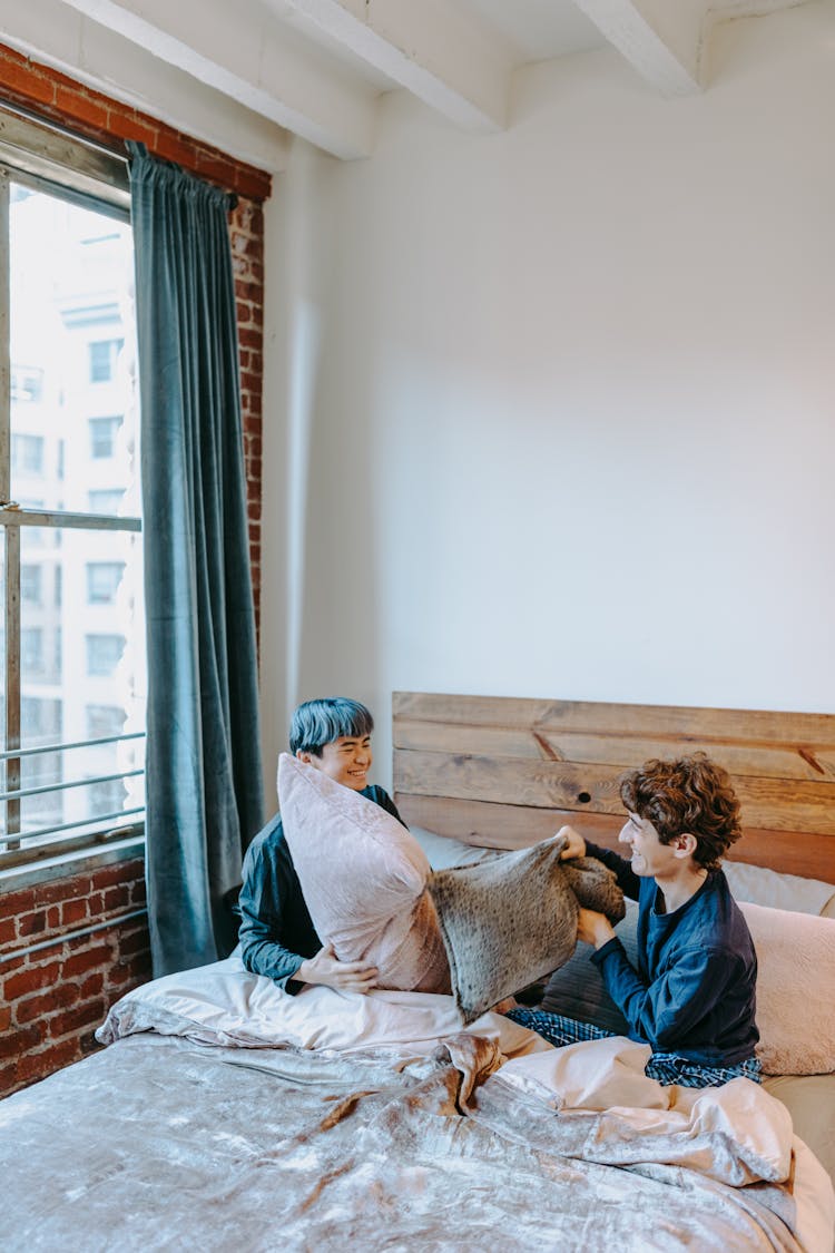 A Couple Pillow Fighting On A Bed