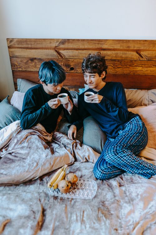 Free Two adults enjoying a cozy breakfast in bed with coffee and pastries, creating a romantic and intimate moment. Stock Photo