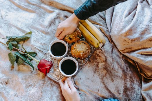 A cozy breakfast tray with coffee, muffins, bananas, and a rose on a bed.