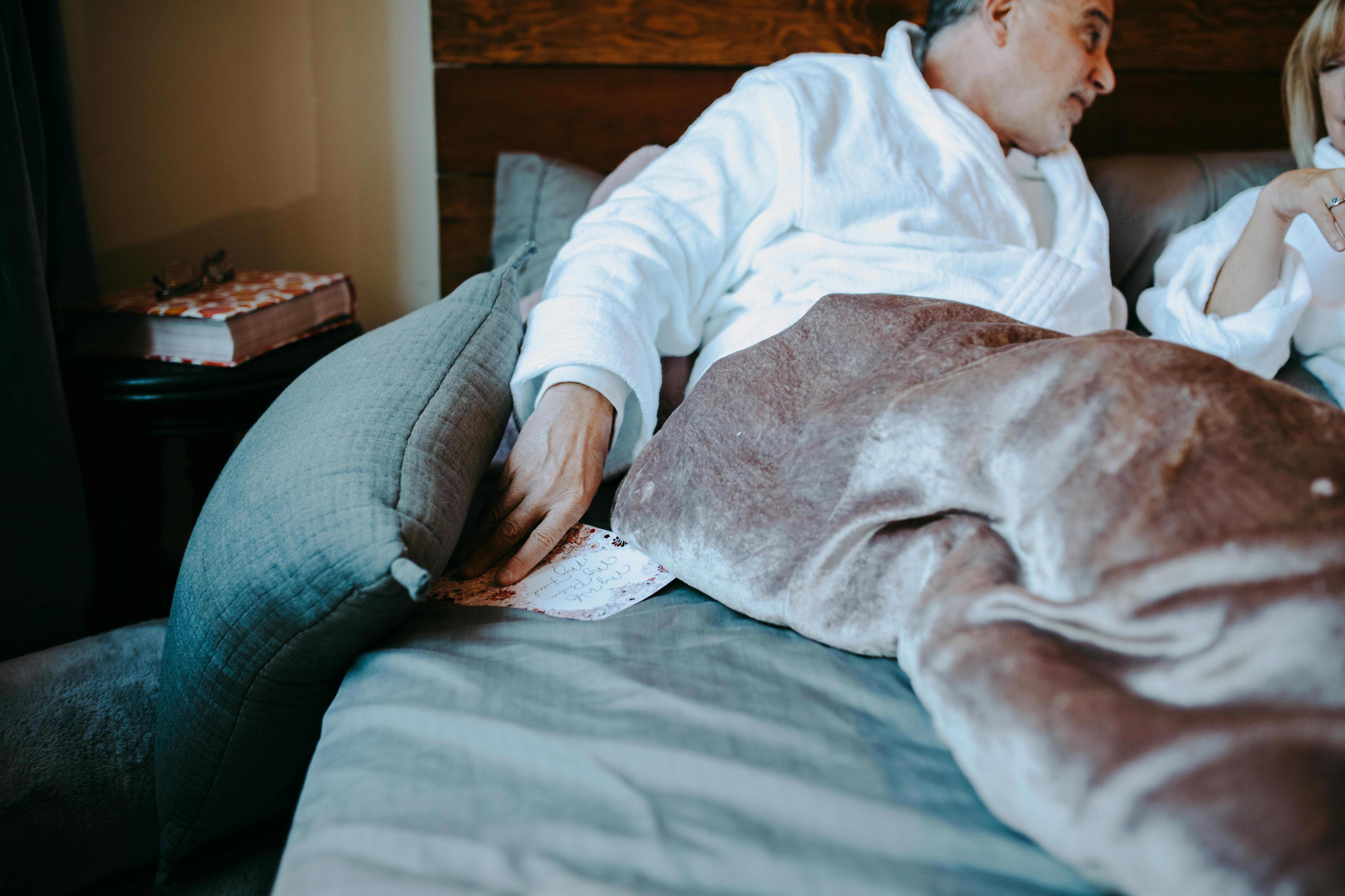 man in white dress shirt and blue denim jeans lying on bed