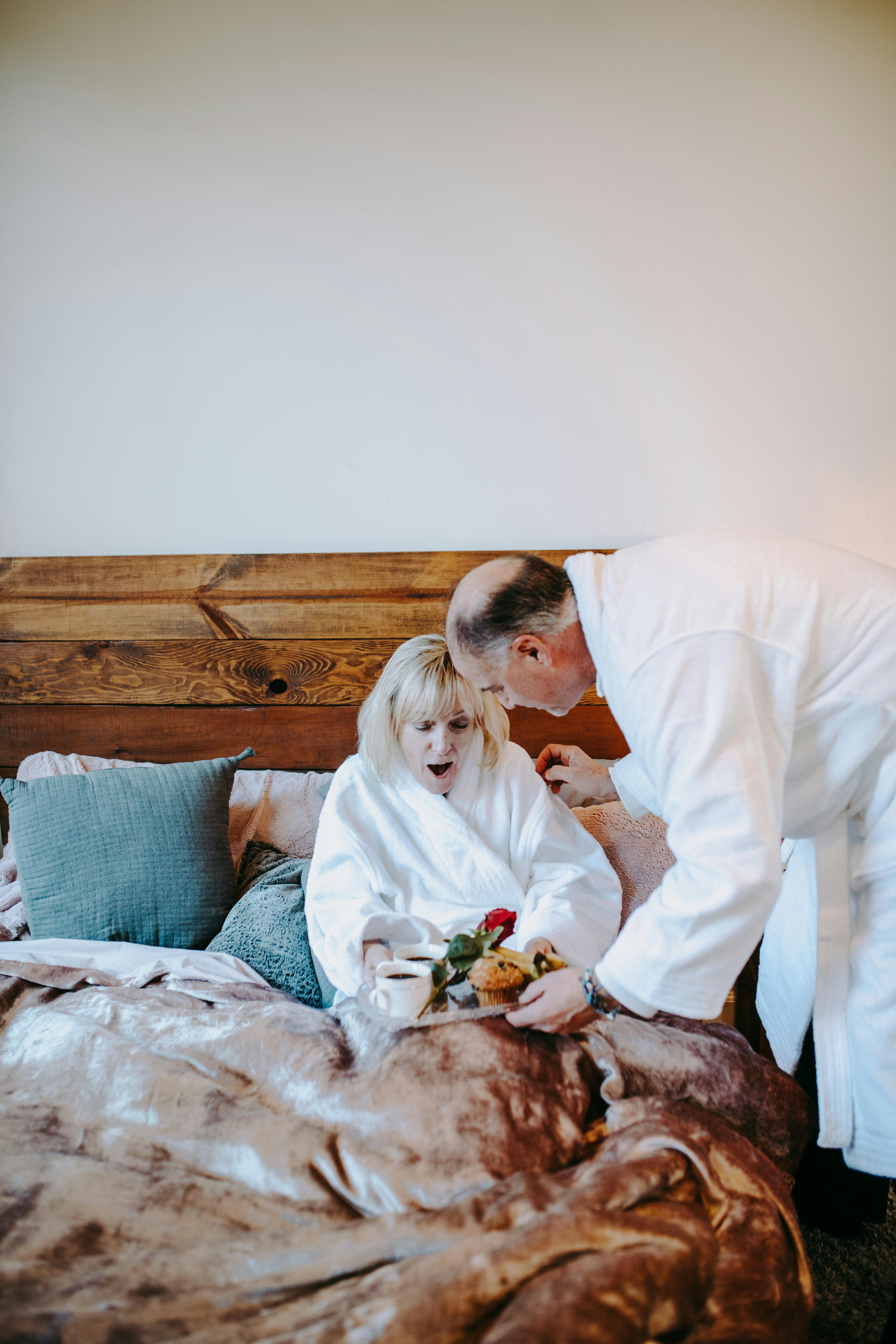 man in white robe sitting on bed beside woman in white long sleeve shirt