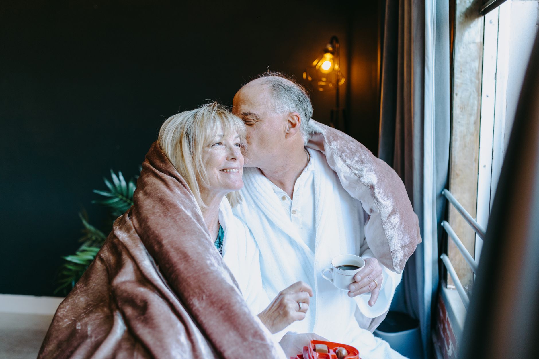 Senior couple sharing a warm embrace over morning coffee by the window.