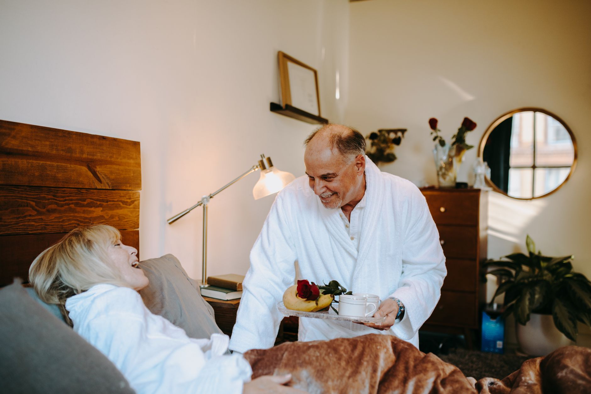 A joyful senior couple sharing a romantic breakfast in bed at home.