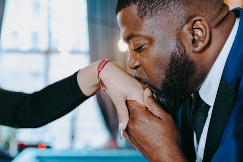 Close-Up Photo of a Man with Facial Hair Kissing Another Woman's Hand