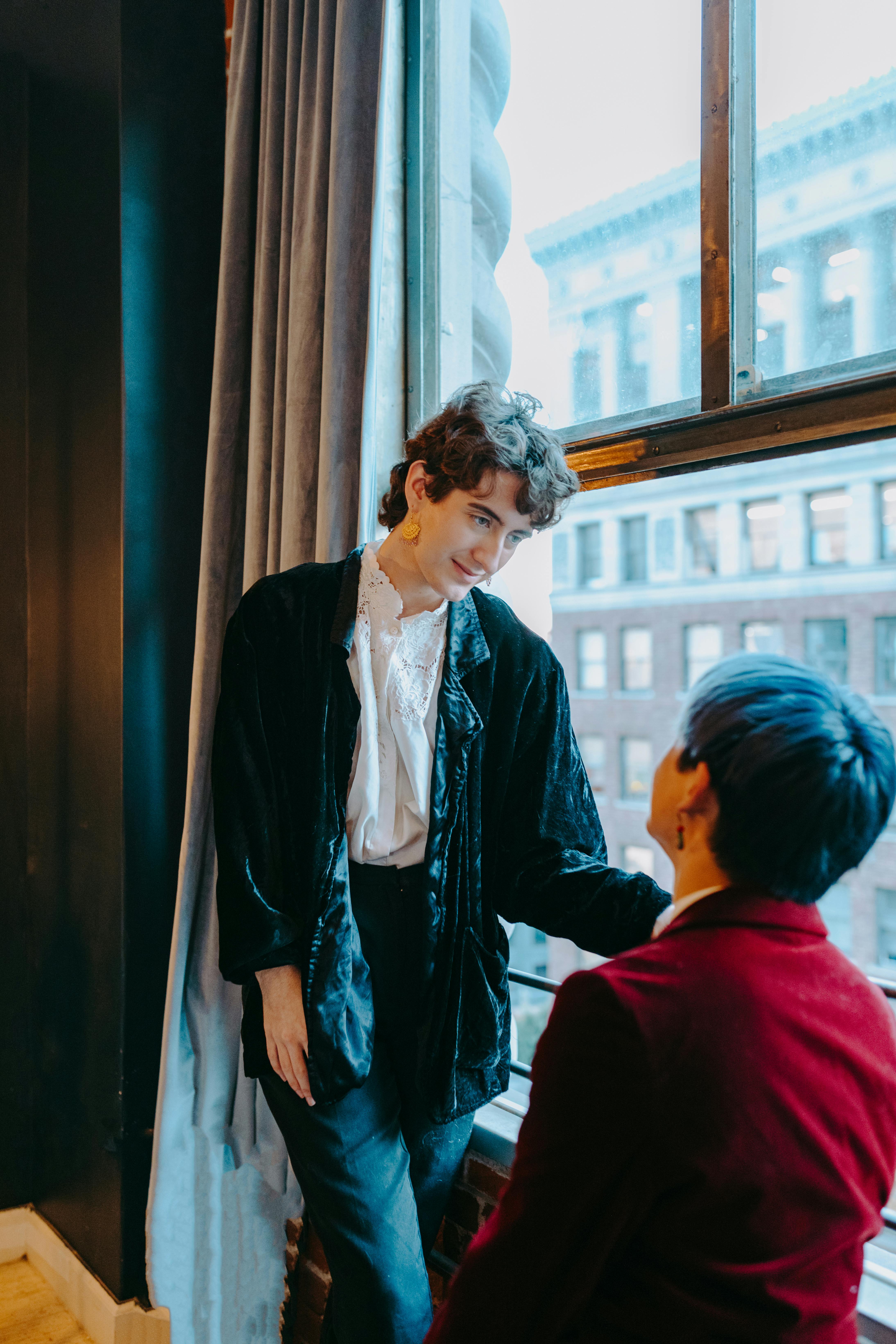 a same sex couple looking at each other while standing near the window