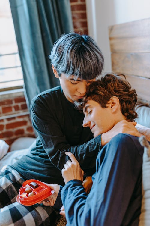 Photograph of a Man with Gray Hair Hugging Another Man on the Bed