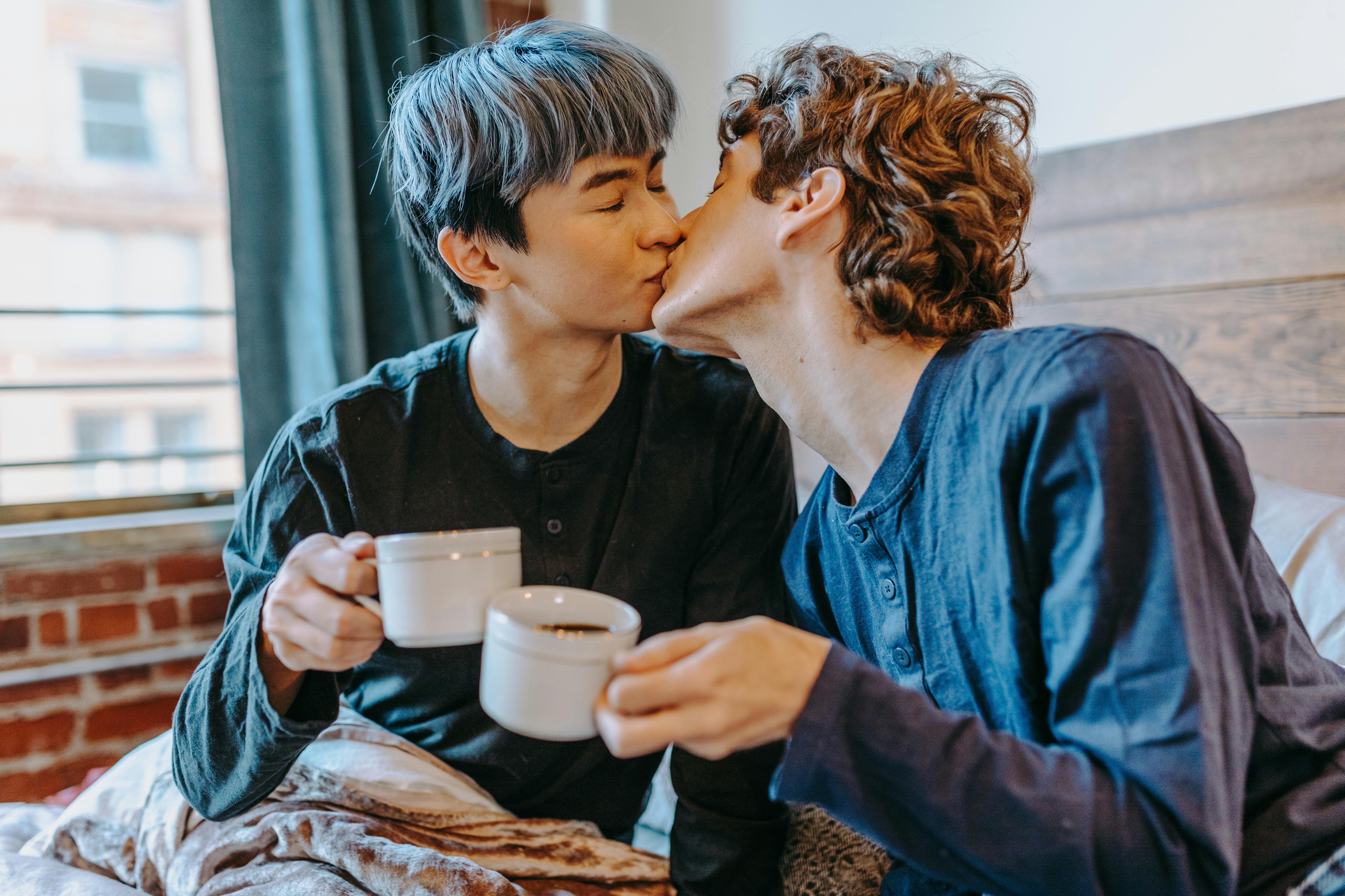 photograph of men kissing while holding cups