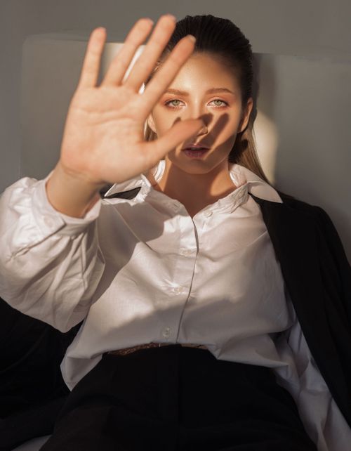Free A woman in a white shirt posing with her hand raised, experiencing soft lighting. Stock Photo