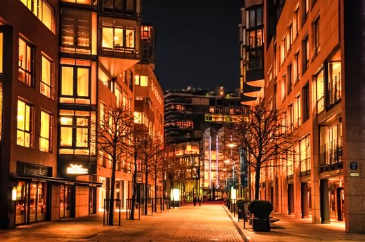 A vibrant city street at night with illuminated modern buildings and trees.
