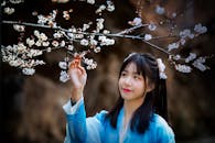A Woman in Blue Long Sleeves Touching Cherry Blossoms on a Branch