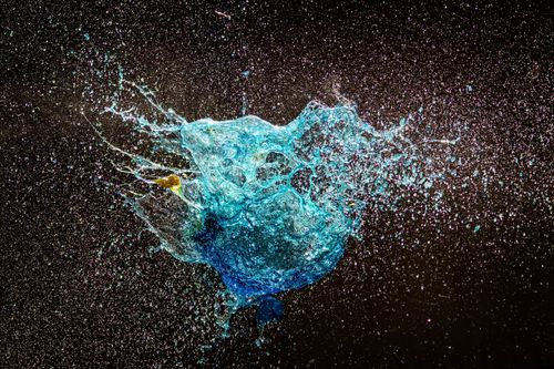 Free High-speed capture of a vibrant blue water splash against a dark backdrop, showcasing fluid dynamics. Stock Photo