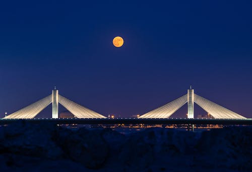 Illuminated Bridge Under a Full Moon on a Blue Sky