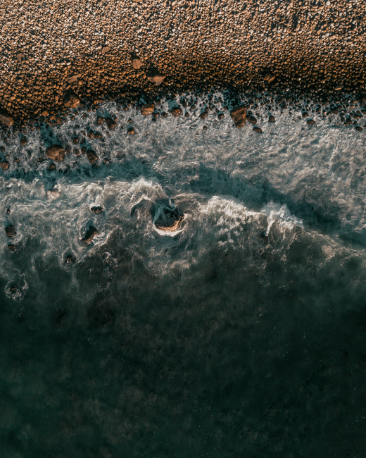 Stunning aerial view of Cape Town's rocky coastline with crashing waves and pebbled shore.