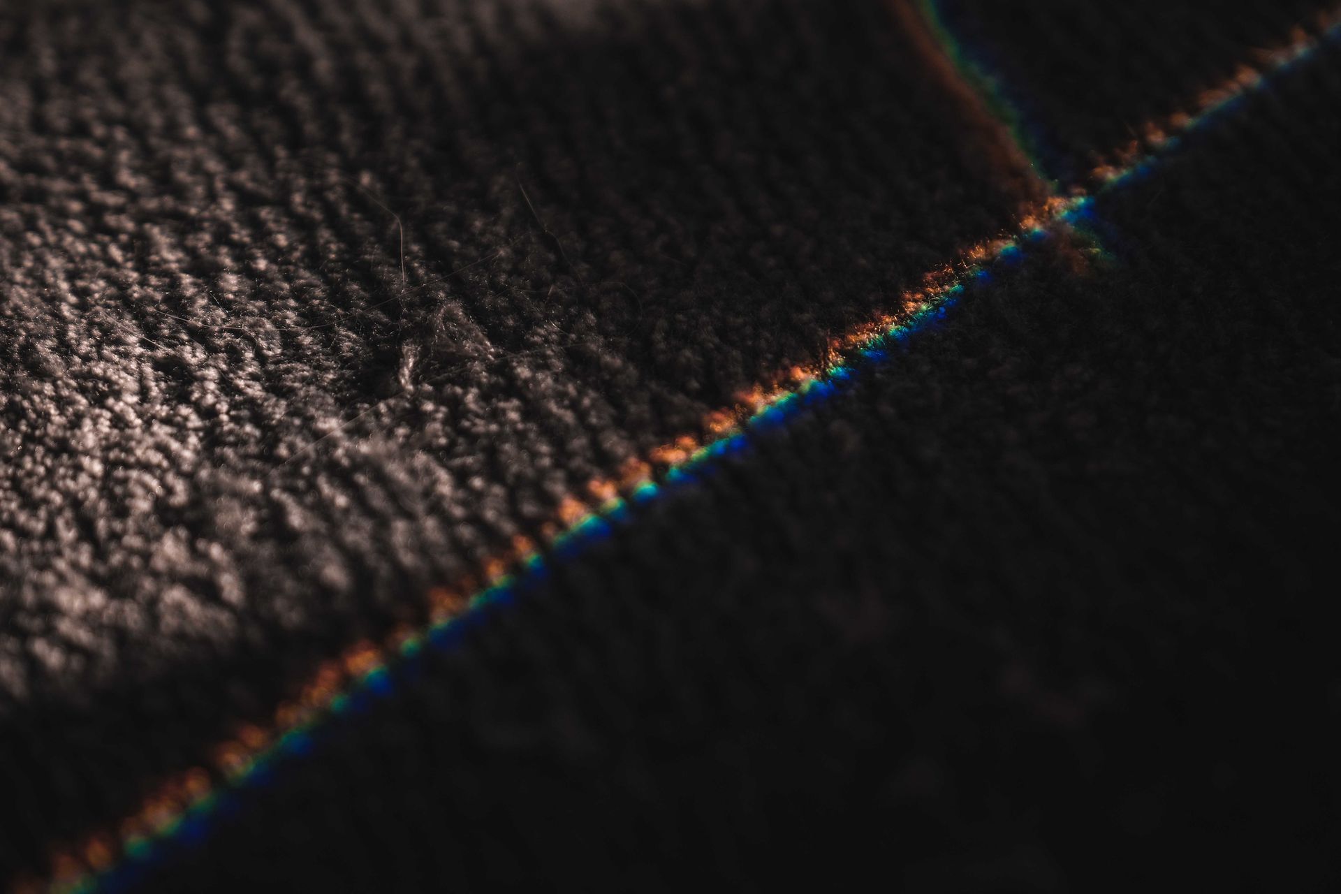 Close-up image of a textured dark surface with a prism of light creating a colorful line.