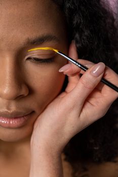 A woman delicately applies yellow eye makeup with a brush.