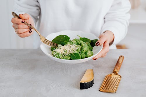 Person Holding Stainless Steel Fork and Green Vegetable on White Ceramic Bowl