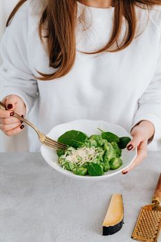 A woman holds a plate of spinach gnocchi, topped with parmesan, showcasing a healthy Italian meal.