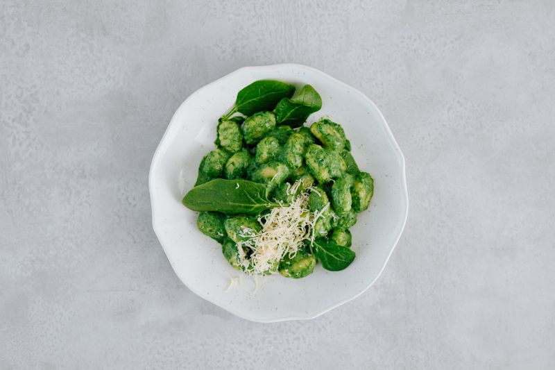 Bowl of green gnocchi with spinach and shaved cheese — photo by Kaboompics on Pexels