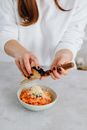 Person in White Long Sleeve Shirt Holding Black and Silver Knife Slicing Food on White Ceramic