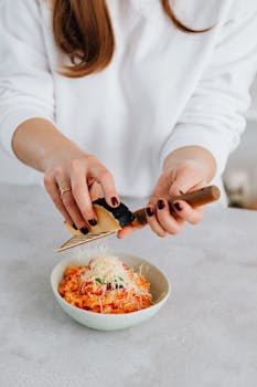 A woman grates parmesan cheese onto a bowl of fresh tomato risotto, showcasing Italian cuisine.