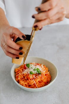 Close-up of a woman grating parmesan over fresh tomato risotto, garnished with basil.