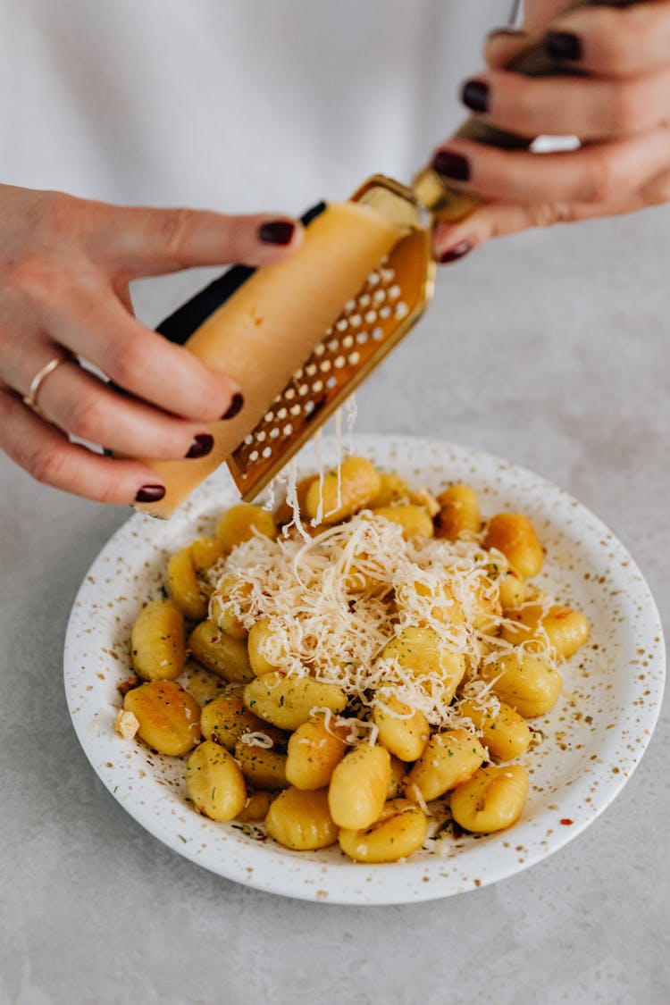 A Person Grating A Cheese On Top Of Gnocchi