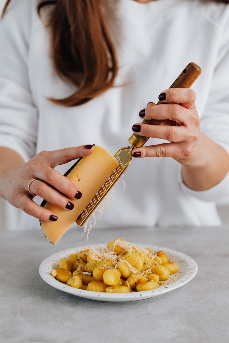 A Person Grating A Cheese On Top Of Gnocchi