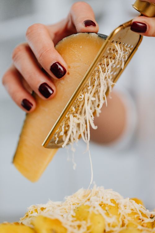 Free A hand grates Parmesan cheese onto pasta, showcasing detailed texture and fresh food preparation. Stock Photo