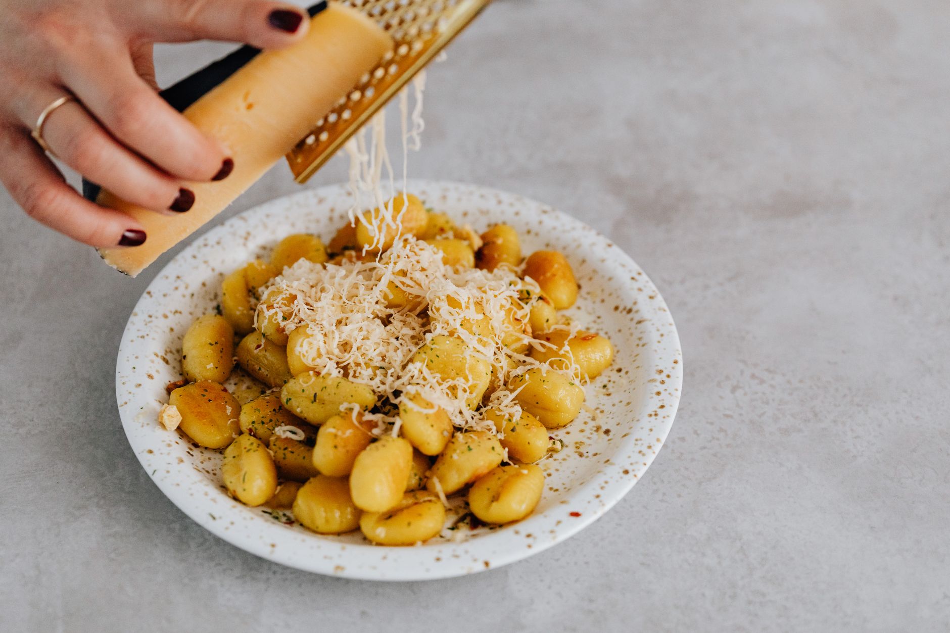 Your Ultimate Weekly Meal Plan for Easy Dinners A ceramic plate of gnocchi with parmesan being grated by hand, highlighting Italian cuisine.