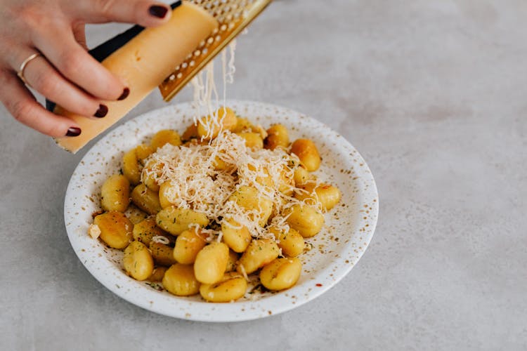 A Person Grating Cheese On A Gnocchi